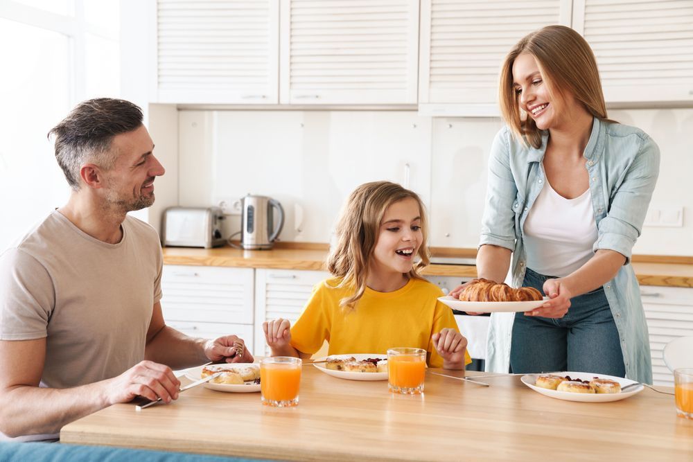 A family is sitting at a table eating breakfast together in the kitchen.