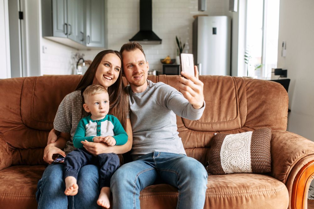 A family is sitting on a couch taking a selfie with a cell phone.