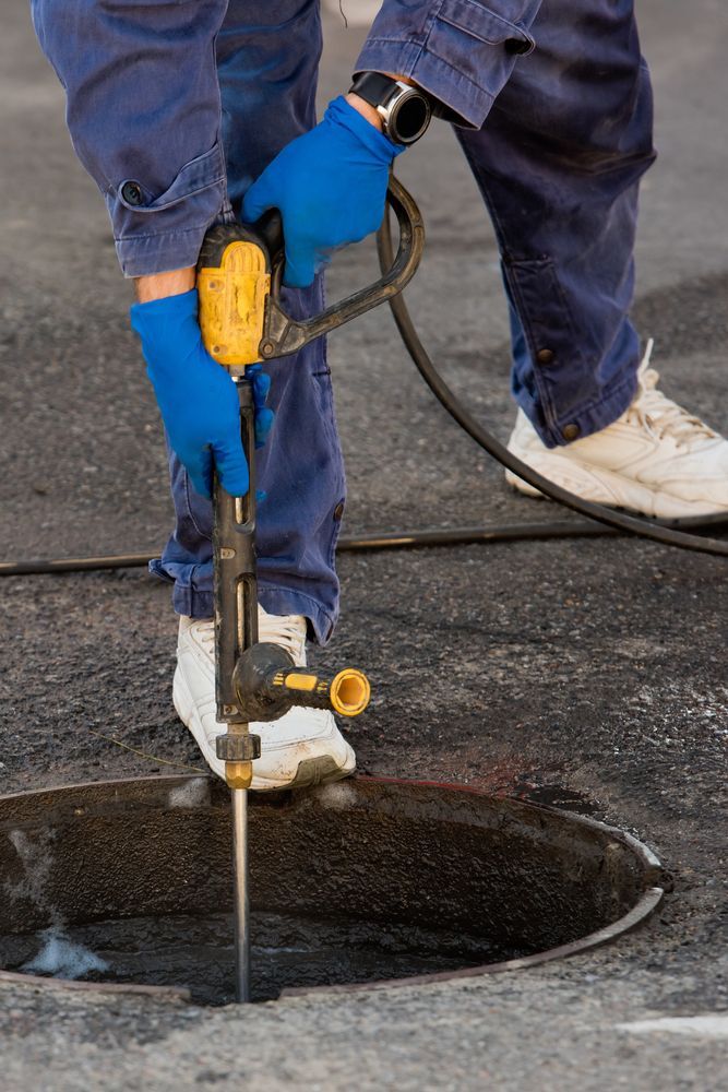 A man is using a drill to drill a hole in a manhole cover.