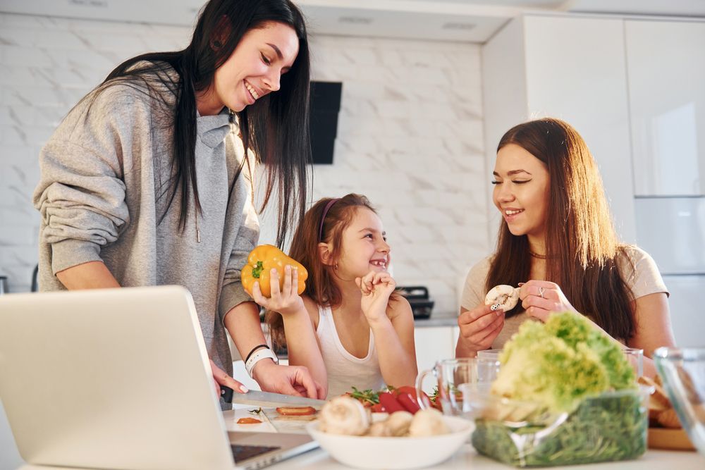 Two women and a little girl are sitting at a table in front of a laptop computer.