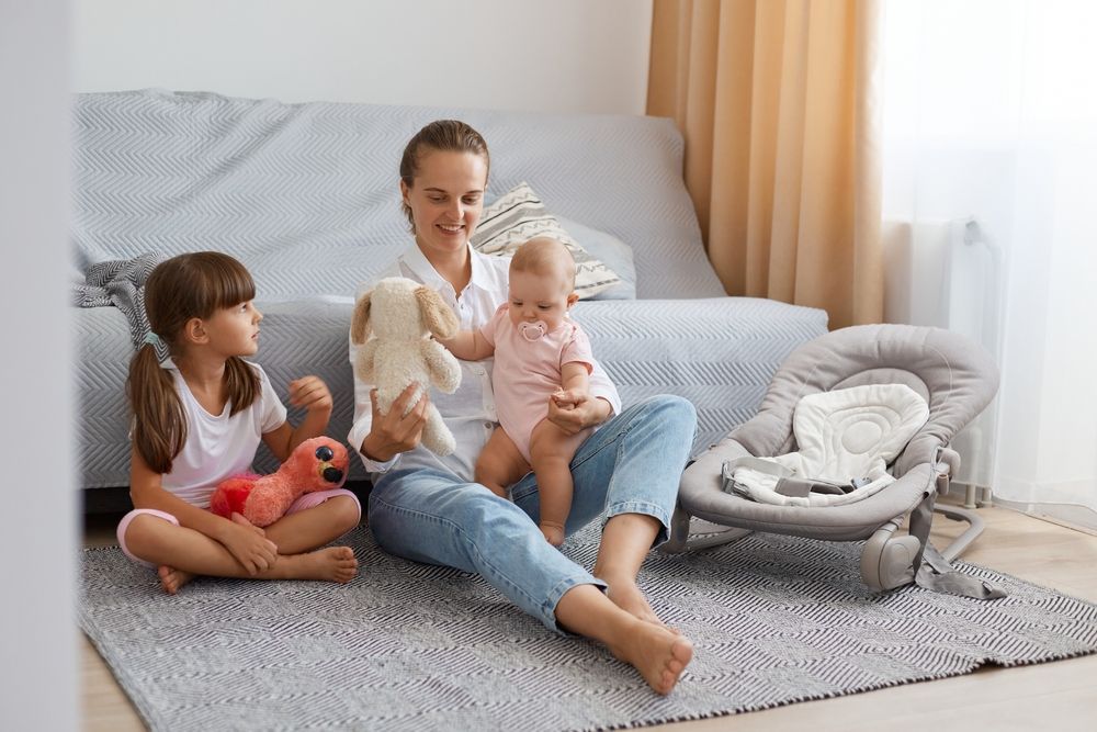 A woman is sitting on the floor with a baby and two little girls.