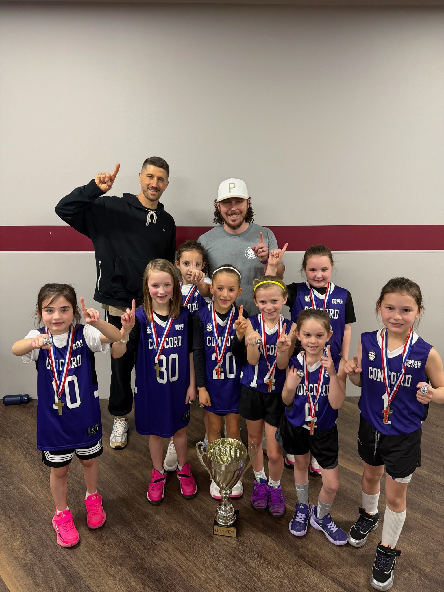 A person wearing a hat and orange shirt, holding a baseball bat on their shoulder on a baseball field.