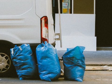 Three blue garbage bags are sitting in front of a white van