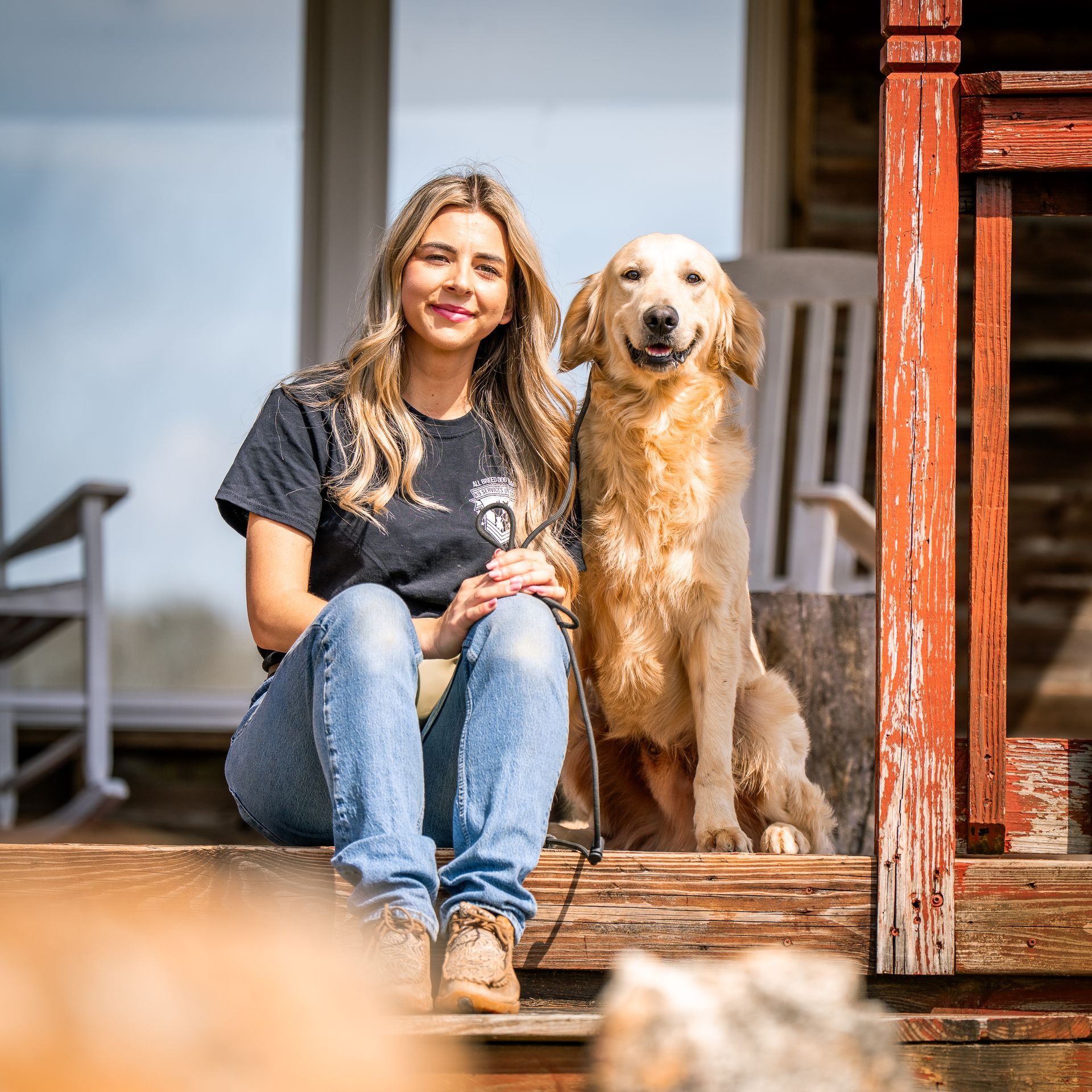 A person and a golden retriever sit side-by-side on wooden porch steps on a sunny day.