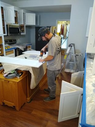 A man is standing in a kitchen painting cabinets.