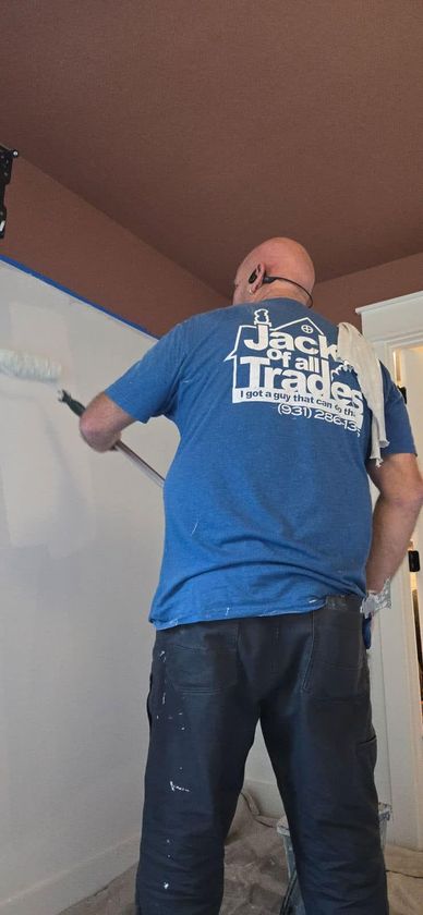 A man in a blue shirt is painting a wall with a roller.