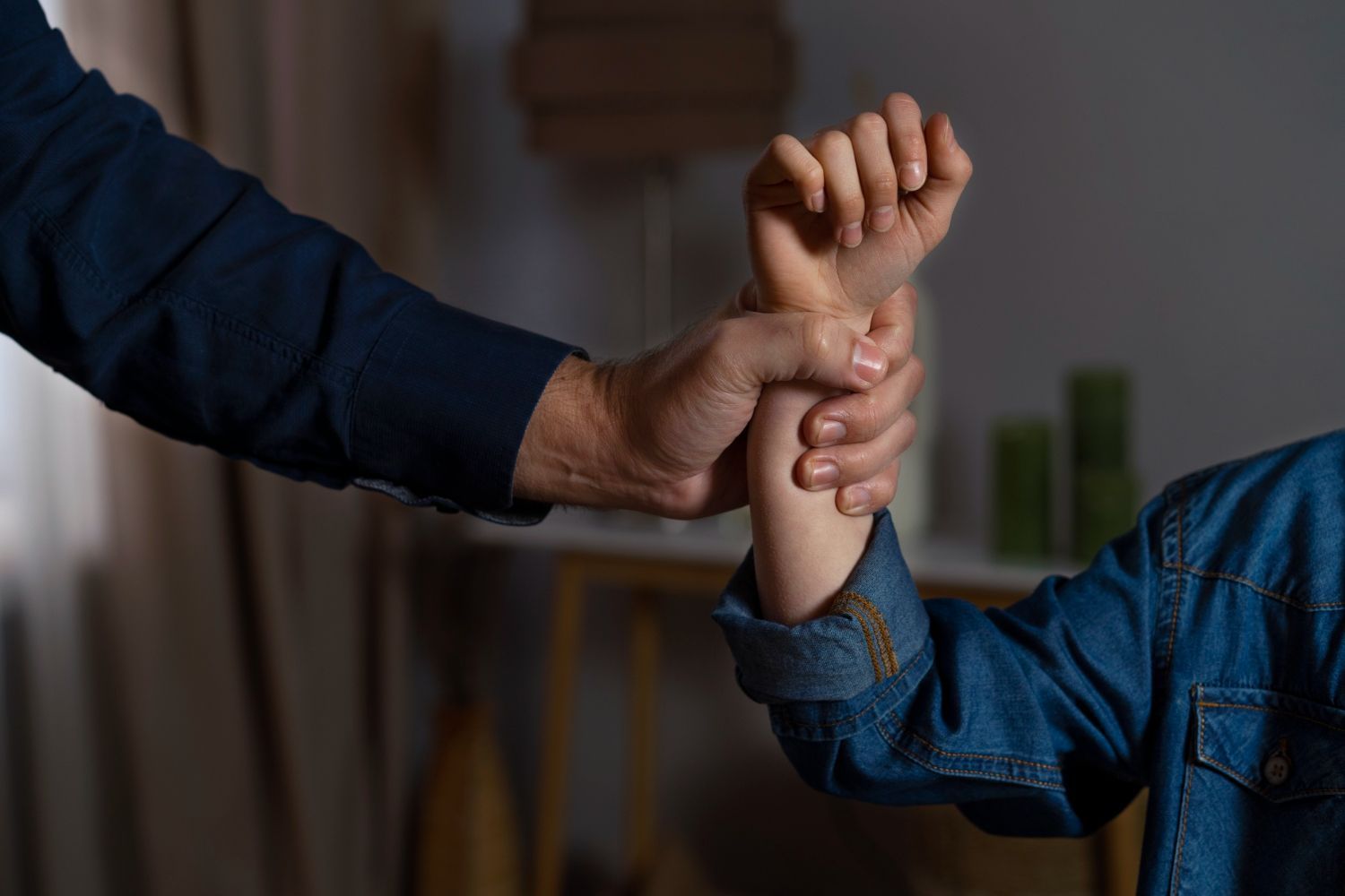Adult holding a child’s wrist gently indoors, both wearing blue denim shirts