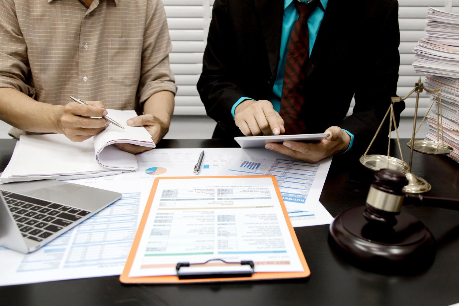 Two people reviewing legal documents at a desk with a gavel, scale, and laptop nearby