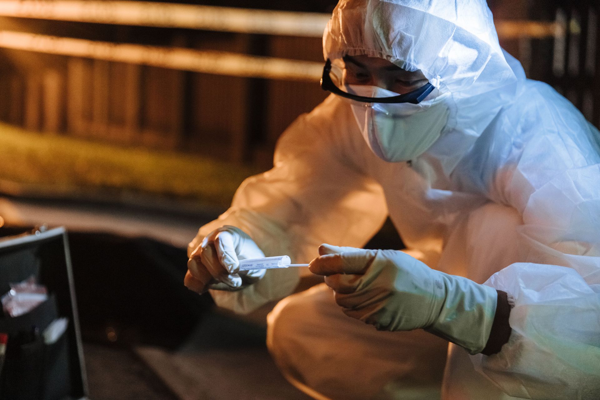 Person in white protective gear and mask handling a sample in a dimly lit lab or field setting