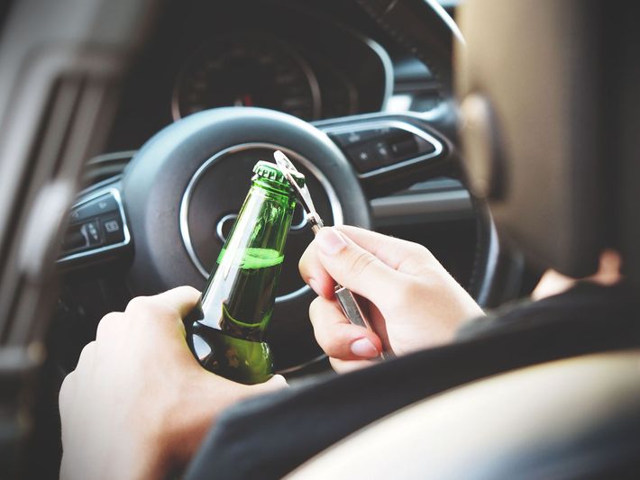 Hands holding a green beer bottle and a key near a car steering wheel