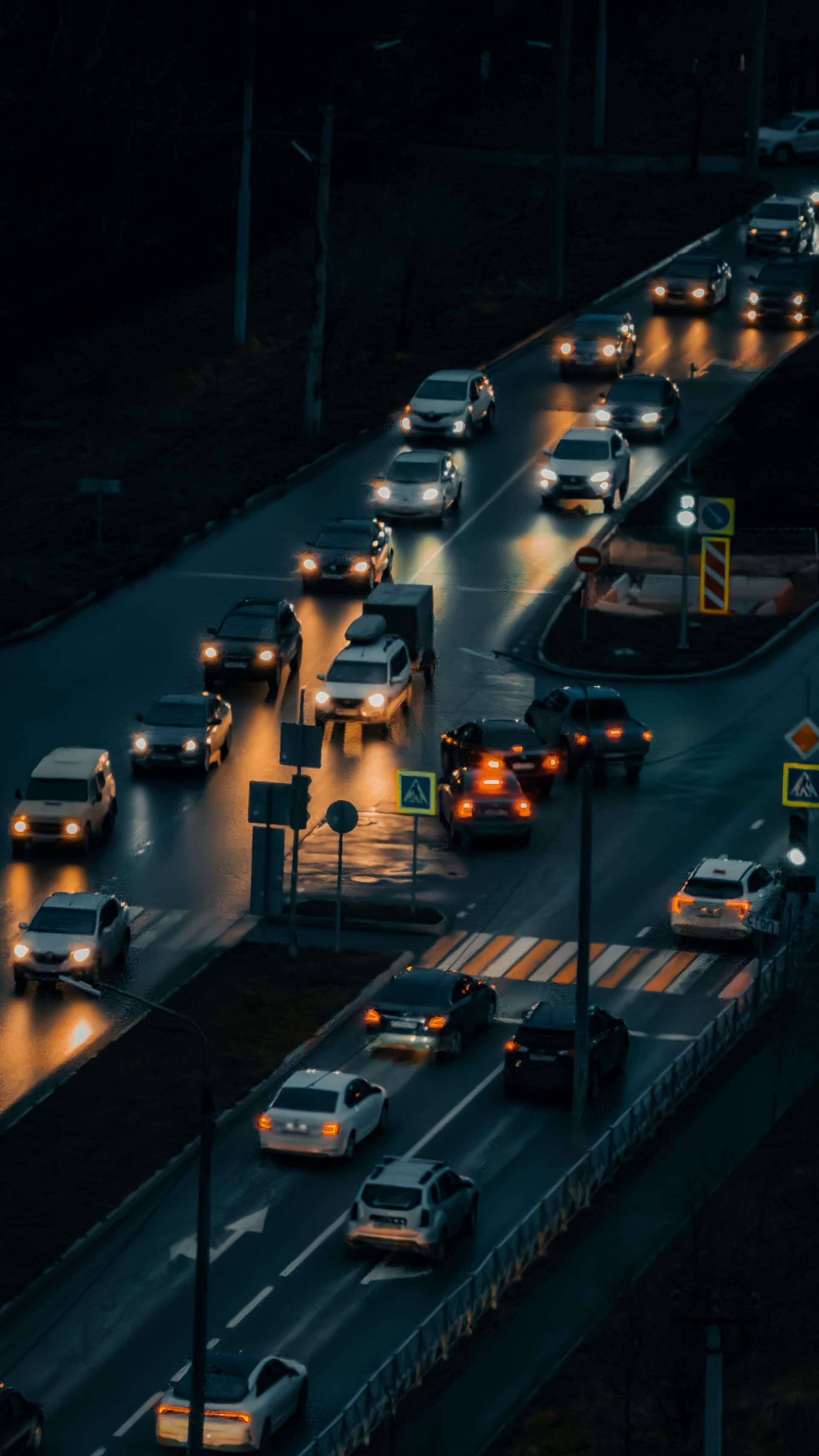 Nighttime traffic on a wet city road, with many cars and headlights reflecting on the pavement.