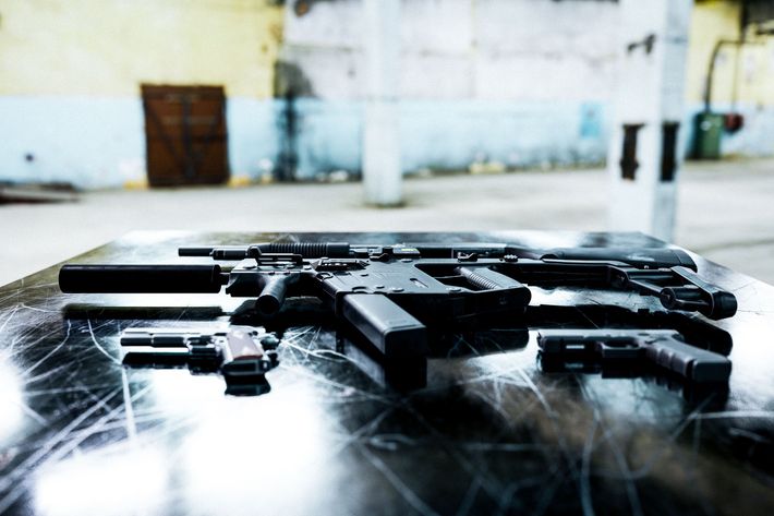 Several black handguns and a rifle laid out on a reflective table in a room