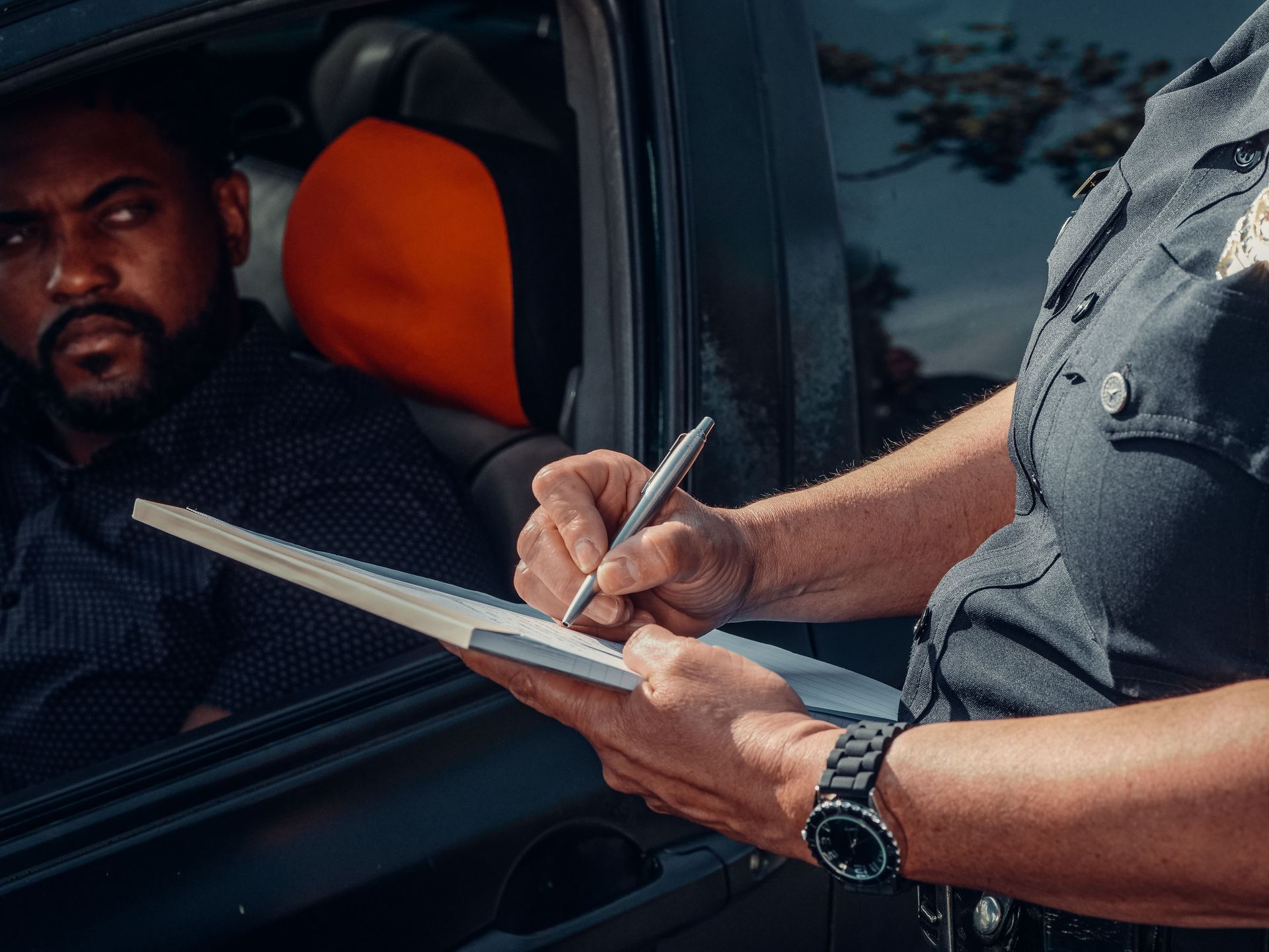 Driver being handed a citation through a car window by a police officer writing on a clipboard