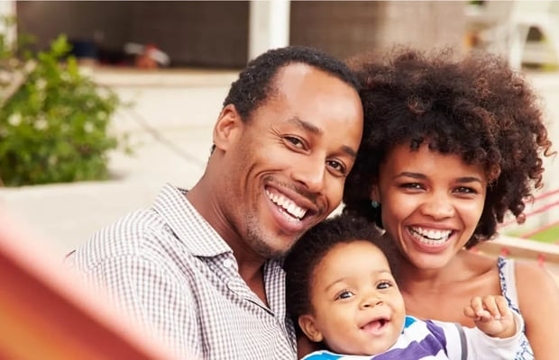 A man and woman are holding a baby and smiling for the camera.