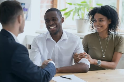 A man and a woman are sitting at a table shaking hands with a man in a suit.