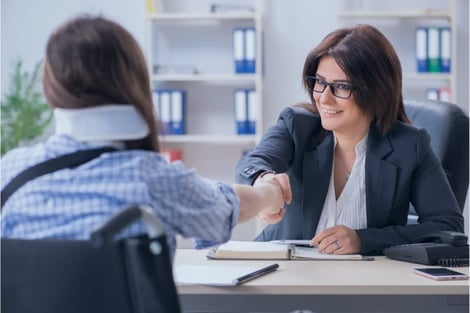 A woman in a wheelchair is shaking hands with a woman in a suit.