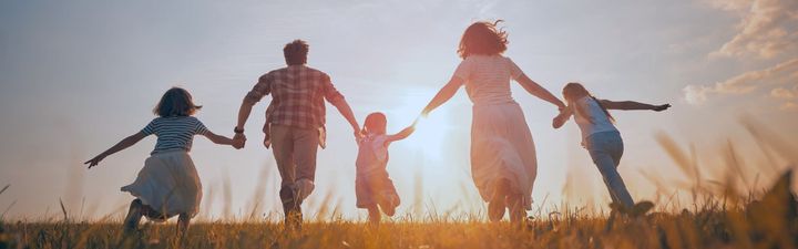 A family is holding hands and running through a field at sunset.