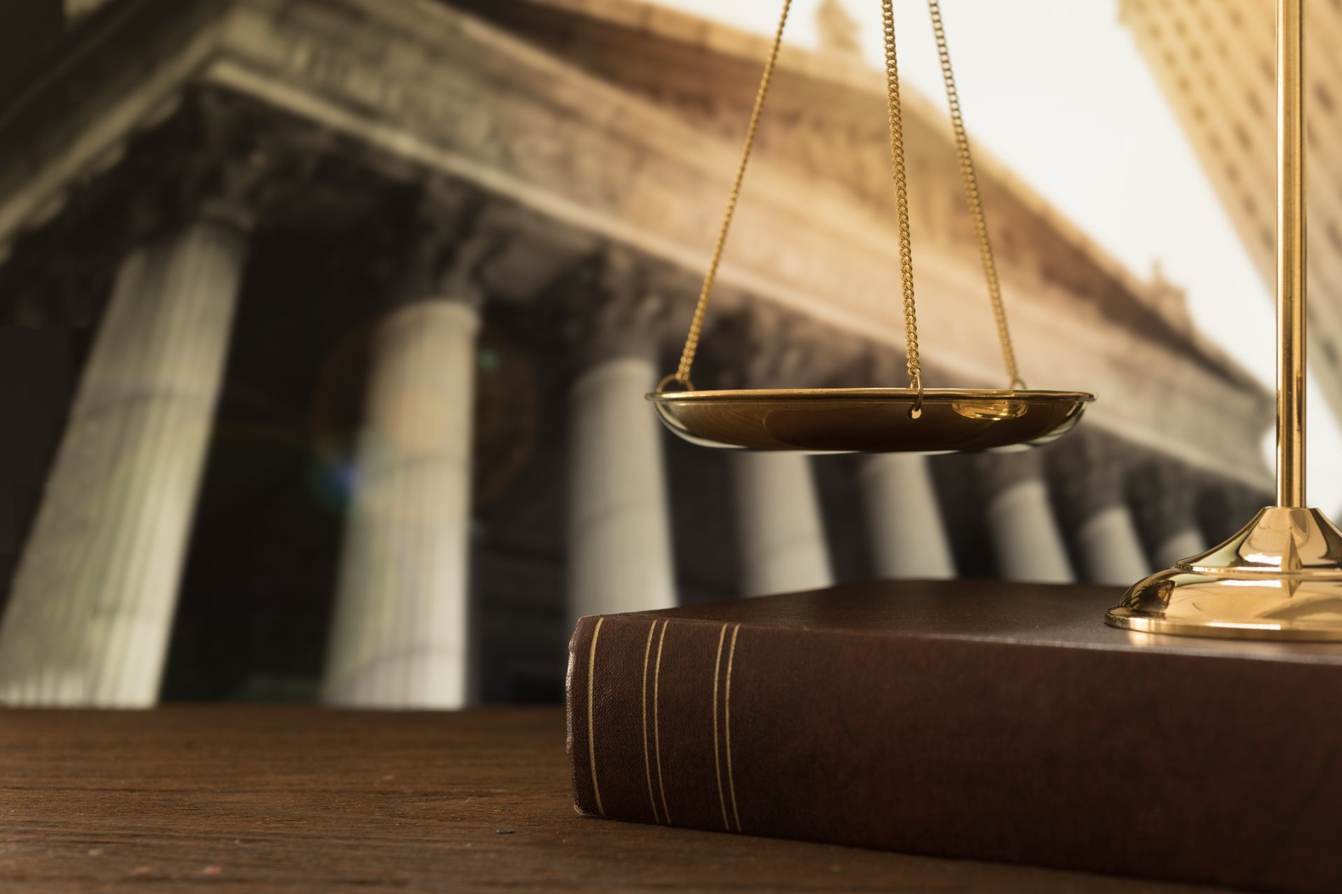 A scale of justice is sitting on top of a book in front of a courthouse.