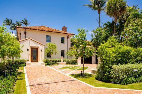 A large white house with a brick driveway and palm trees in front of it.