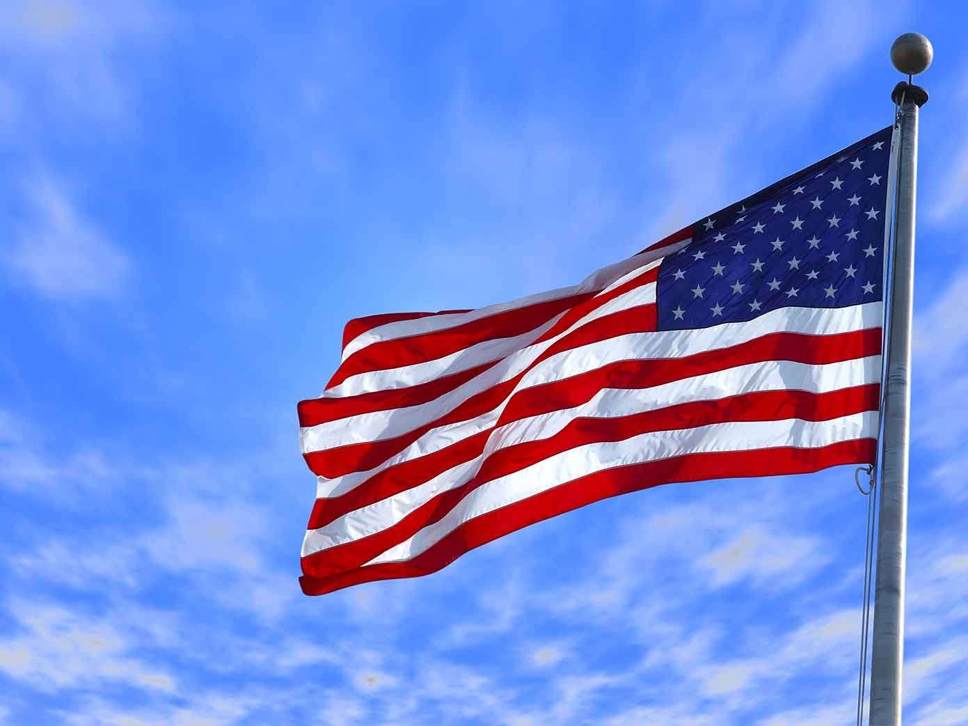 An american flag is waving in the wind against a blue sky