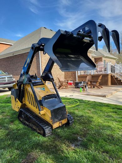 Yellow and black mini skid steer with grapple attachment on a lawn.