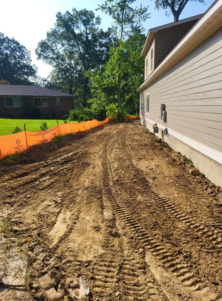 Dirt yard with tire tracks next to a light-colored building. Orange safety fence lines the far side of the yard.