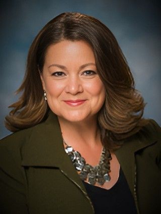 A woman wearing a green jacket and a silver necklace is smiling for the camera.