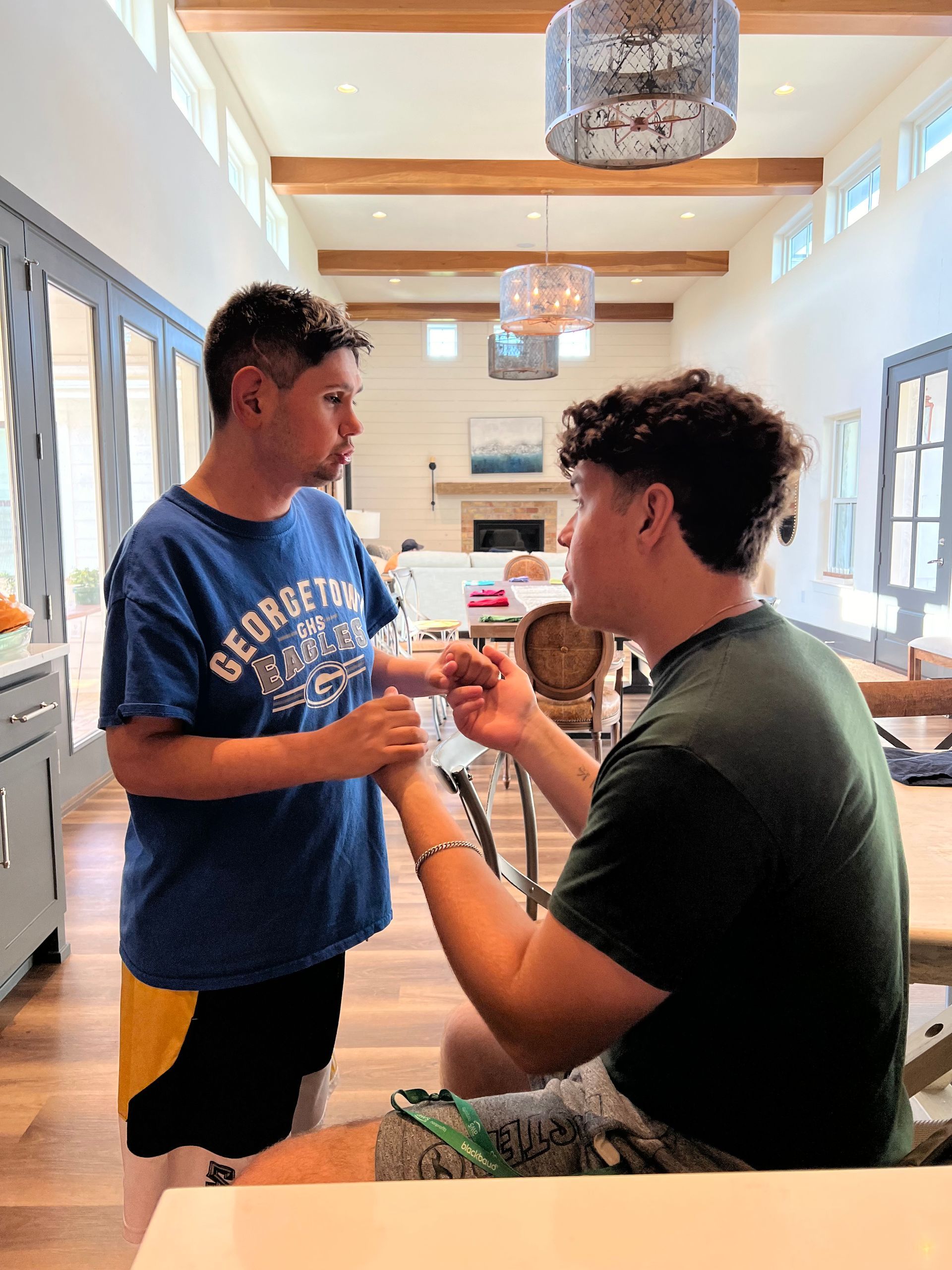 Two men are sitting at a table in a living room talking to each other