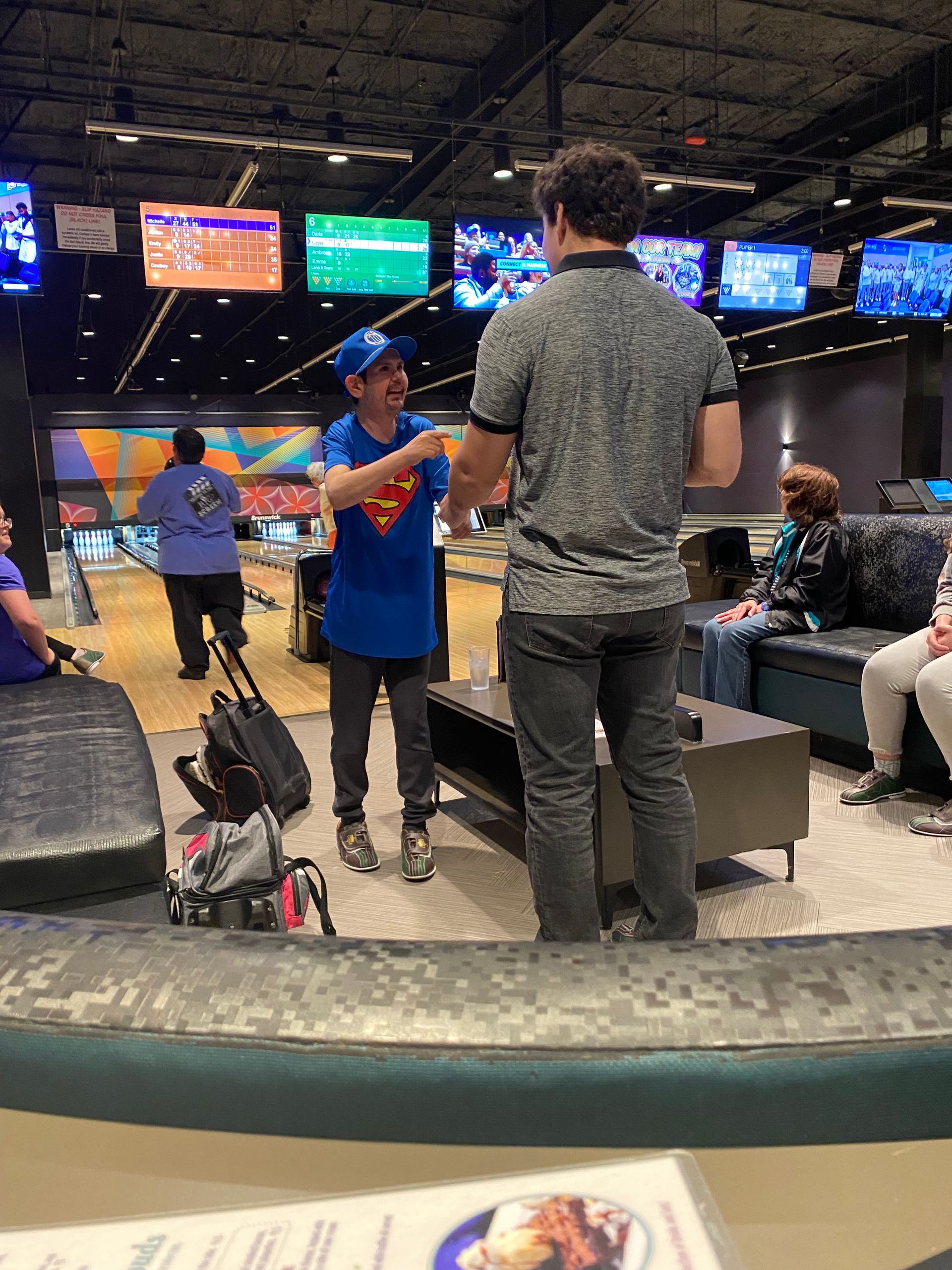 A man in a superman shirt is talking to another man in a bowling alley.