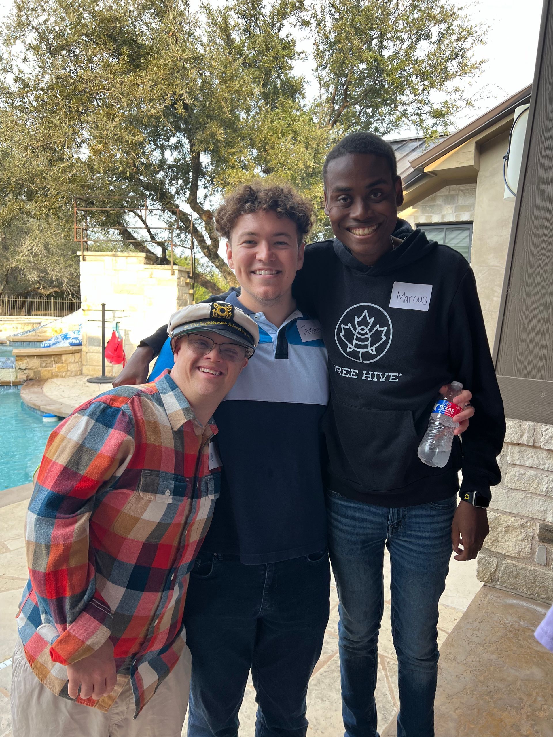 Three young men are posing for a picture in front of a pool.