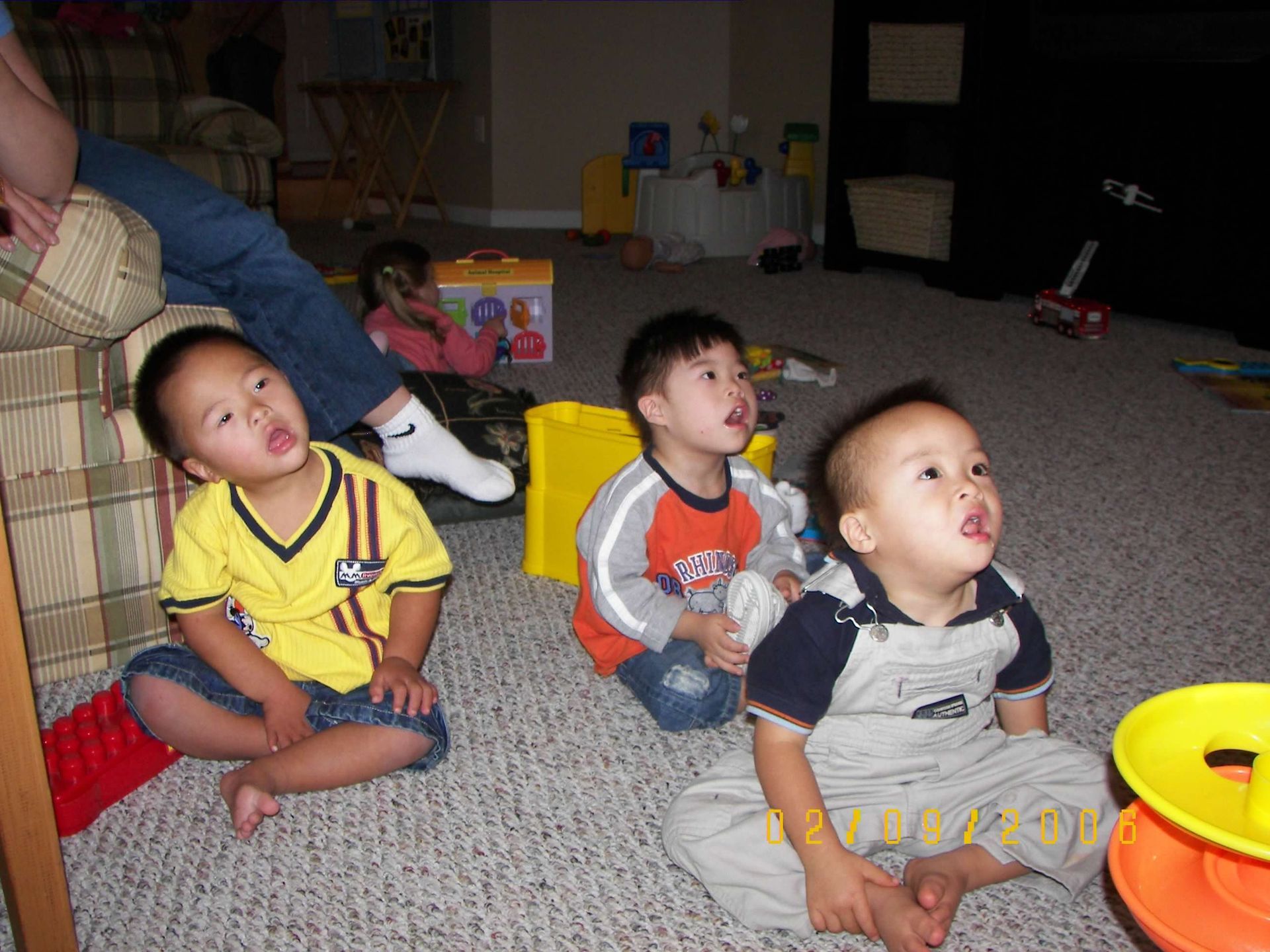 Three young boys are sitting on the floor looking up at something