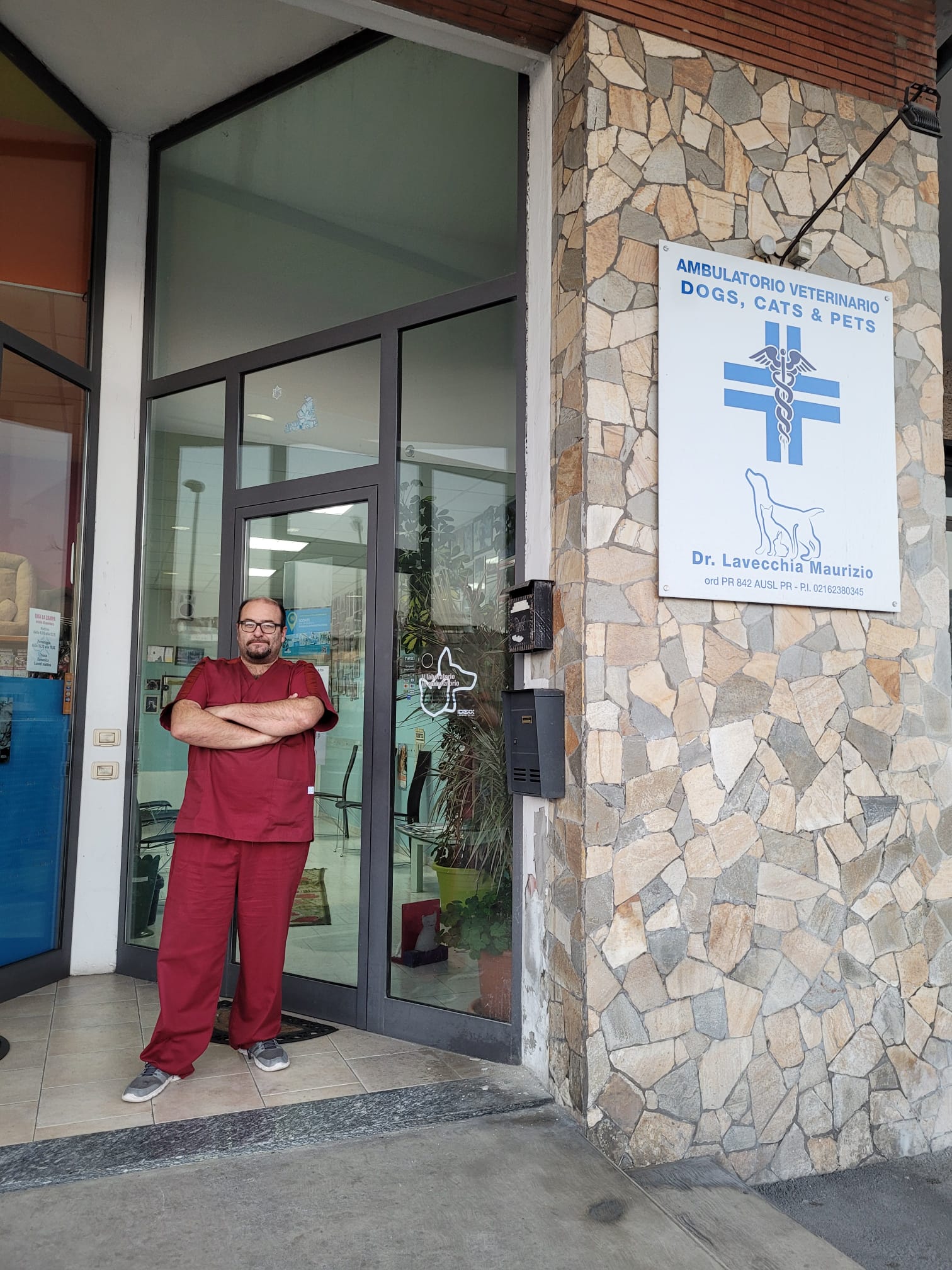 Una persona in camice color marrone è in piedi all'ingresso di una clinica veterinaria con un cartello.