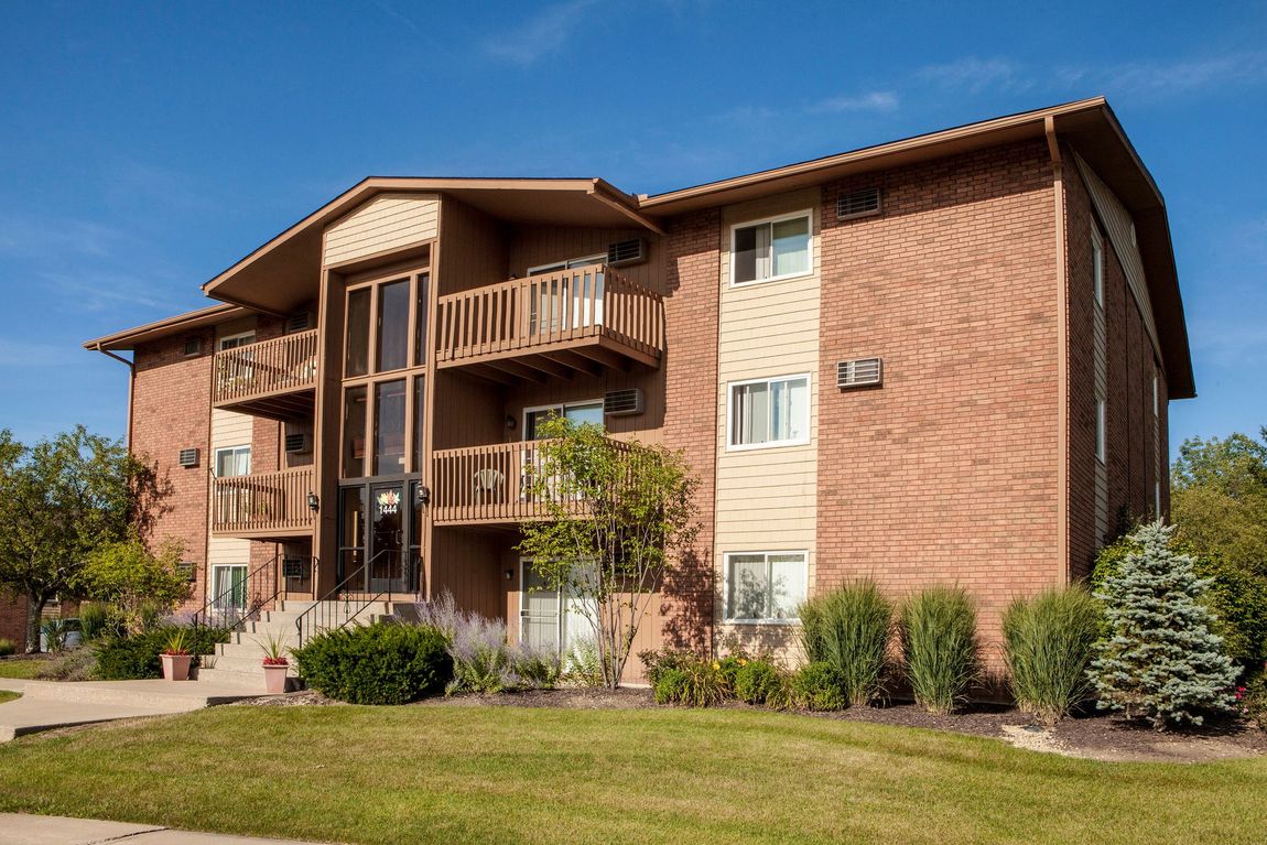 Apartment building with brick exterior, balconies, and green lawn under a blue sky.