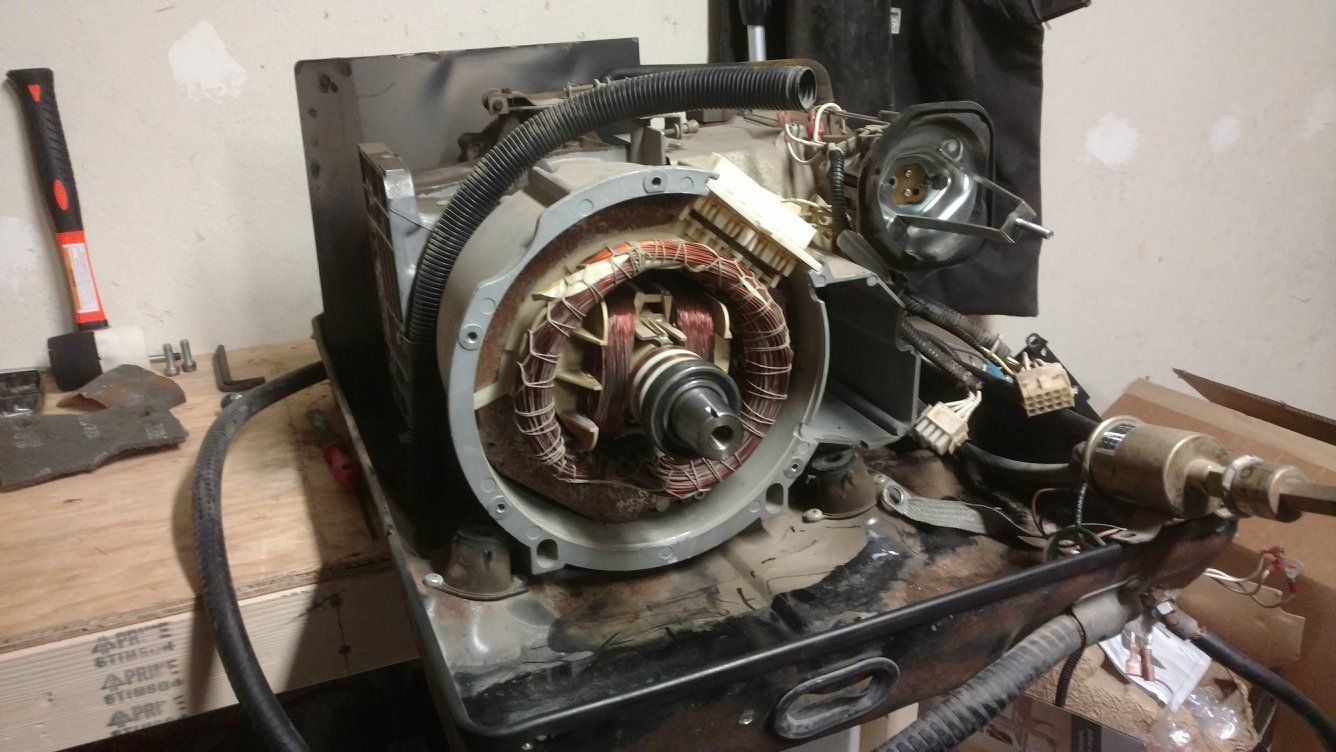 A disassembled generator on a workbench with exposed internal components, including copper windings.