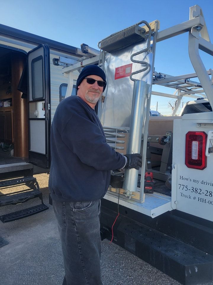 Man in black hat and sunglasses holding a metal panel near a truck, RV in the background. Sunny day.