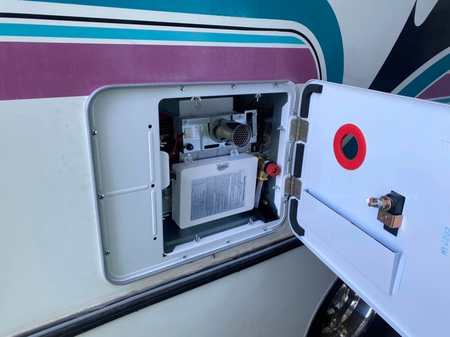 RV water heater access door open, showing components inside a compartment.