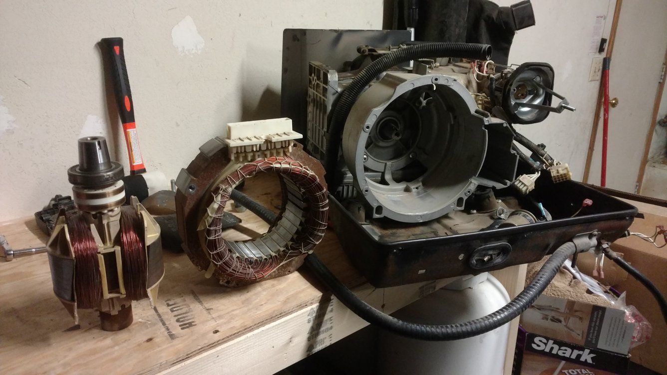 Disassembled air compressor components on a workbench: motor, housing, and coils.