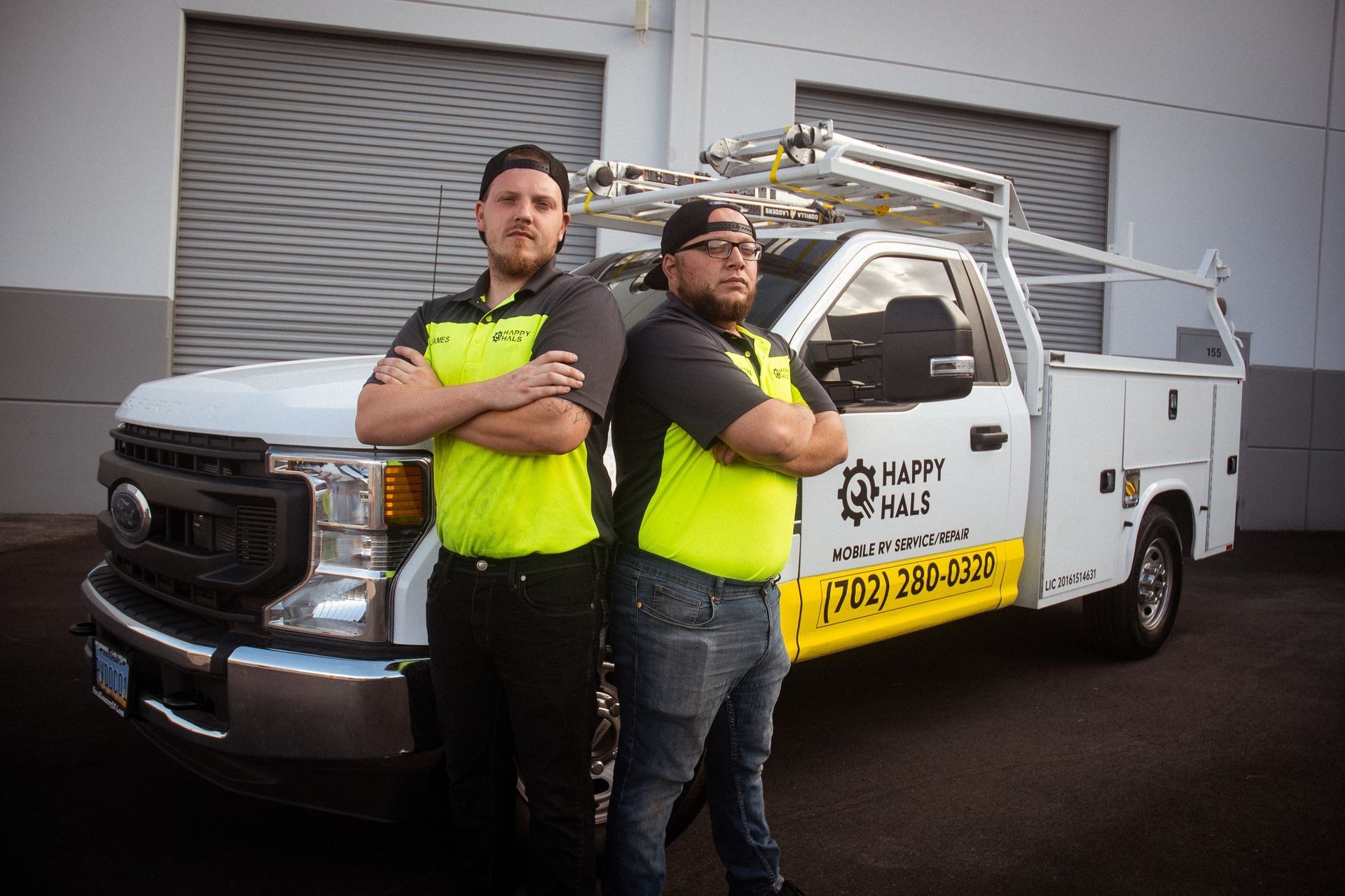 Two men in company shirts stand beside a white work truck.