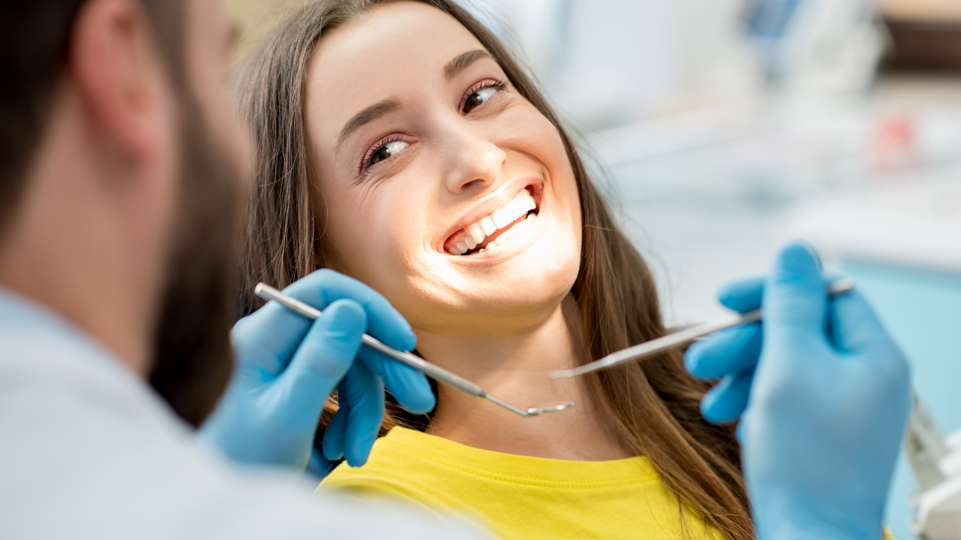A woman is smiling while having her teeth examined by a dentist.