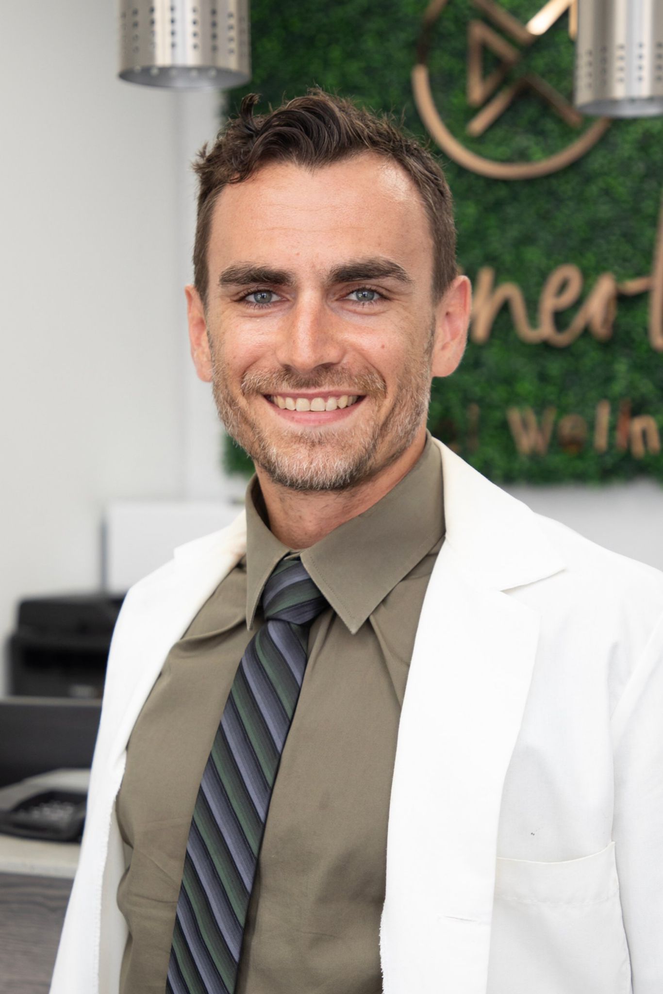 A man in a white coat and tie is smiling for the camera.