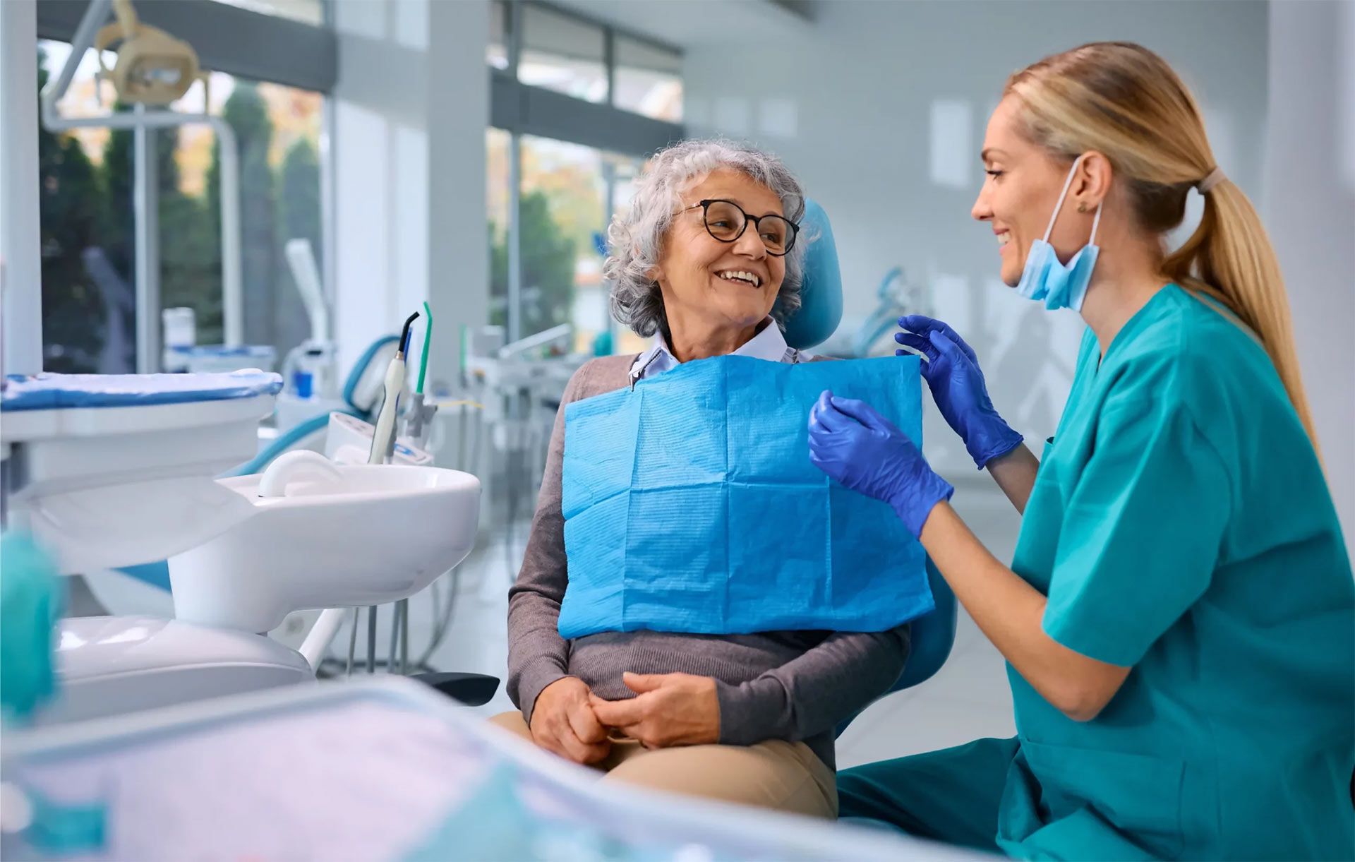 An elderly woman is sitting in a dental chair talking to a dentist. - dental implants