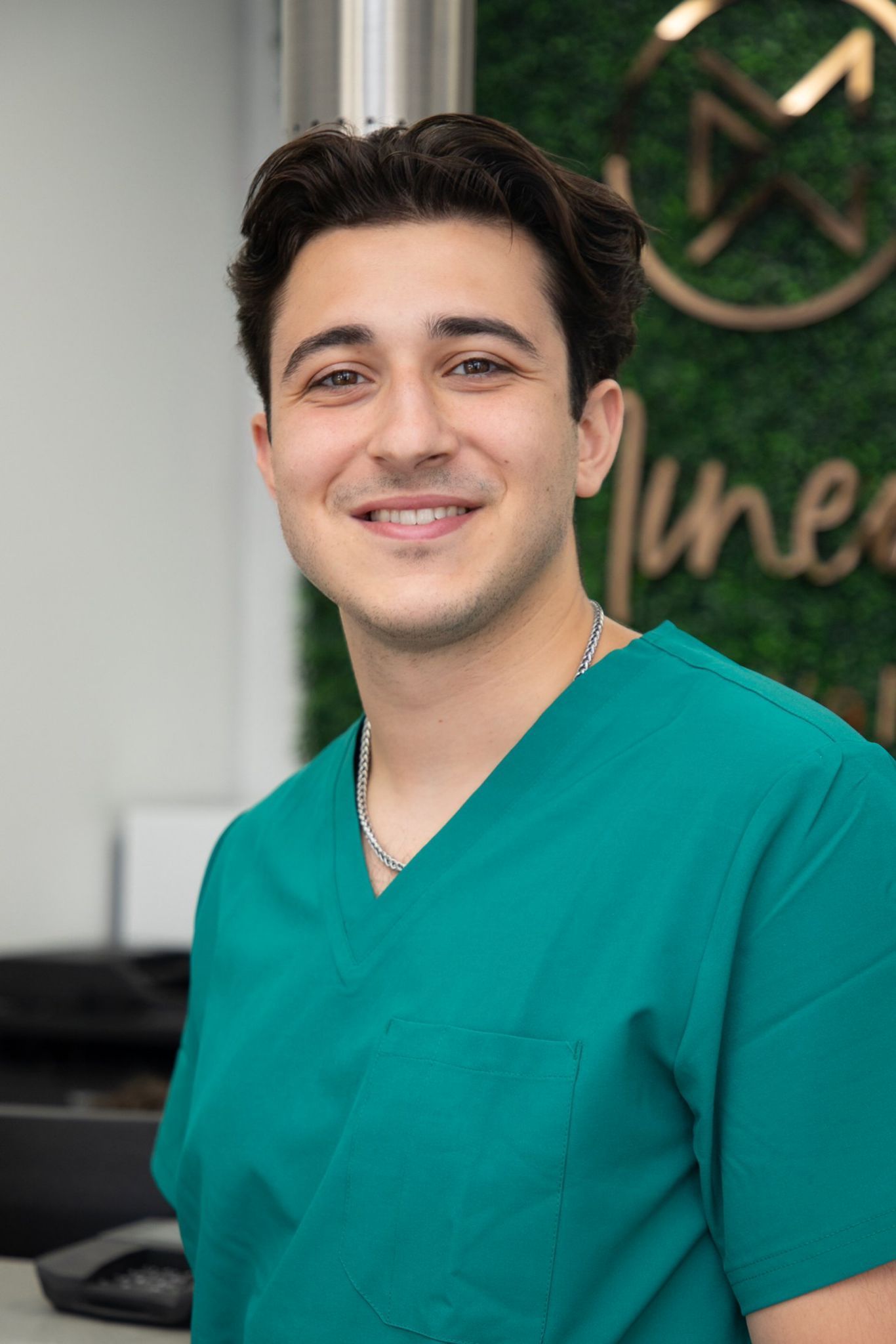 A young man in a green scrub top is smiling for the camera.