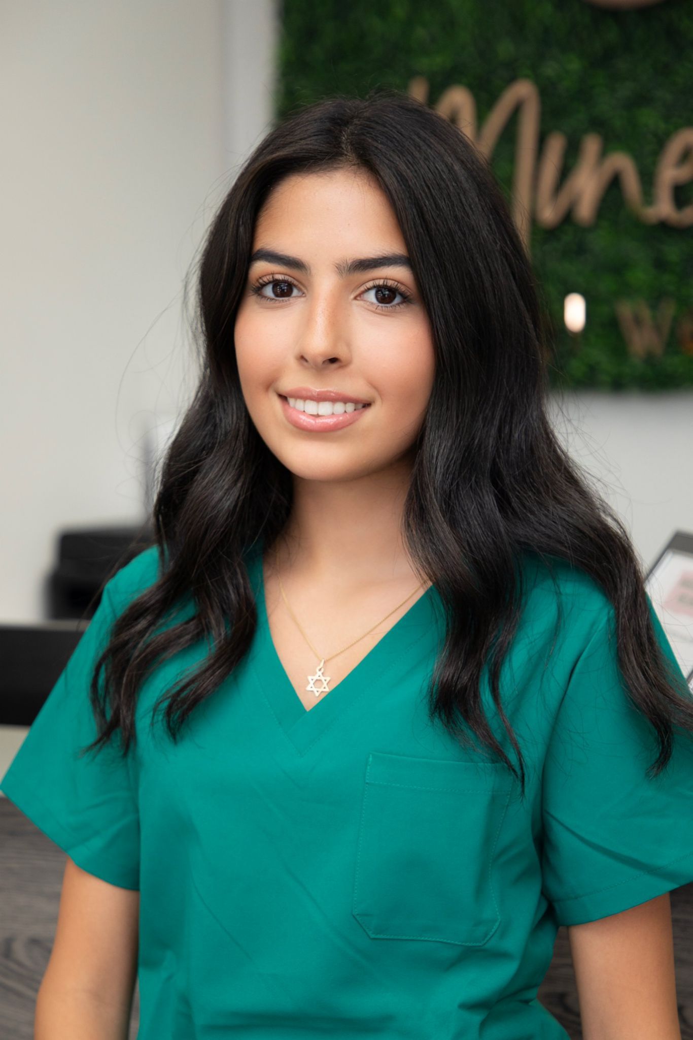 A woman in a green scrub top is smiling for the camera.