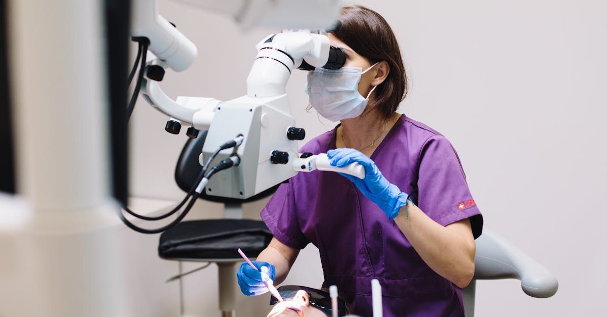 A female dentist is examining a patient 's teeth under a microscope. - biomimetic dentistry