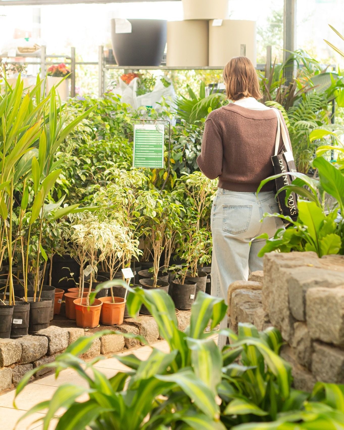Mujer comprando plantas en un centro de jardinería, mirando el follaje verde, frente a las plantas en macetas.
