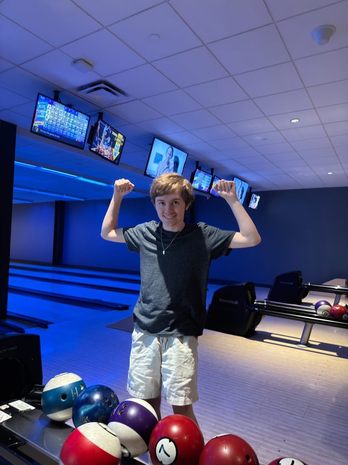 Man in red shirt and blue hat smiles at a bowling alley.