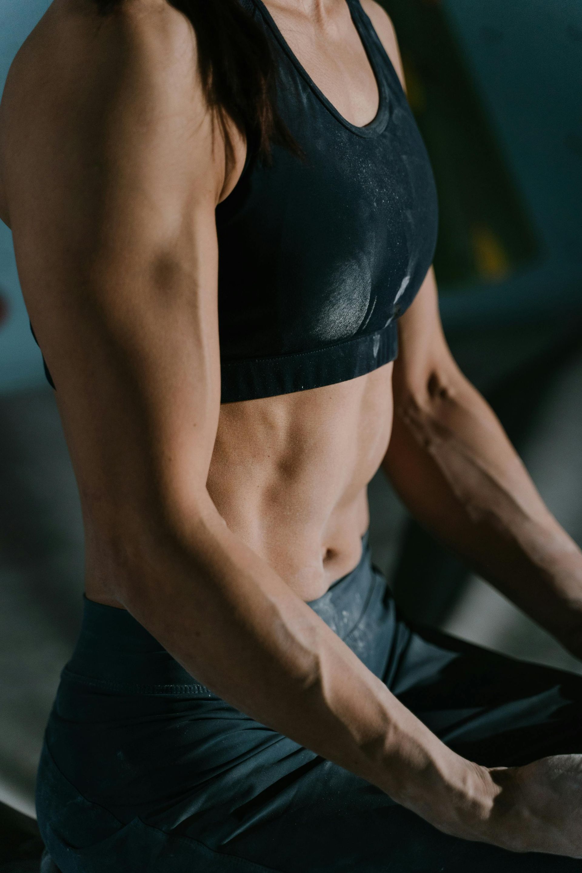 A woman in a black sports bra and black pants is sitting down.