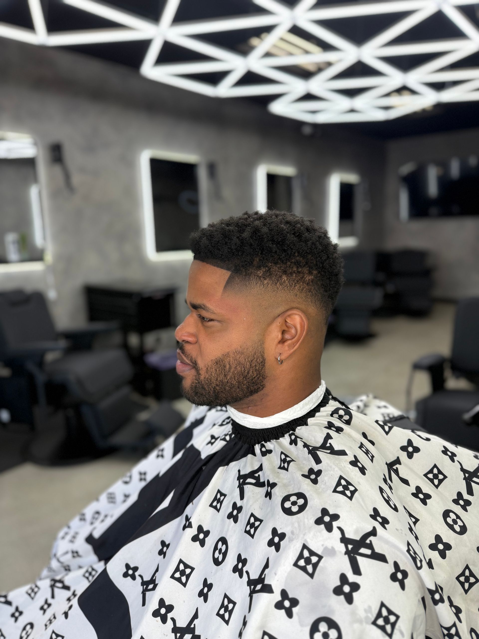 A person with a clean skin fade haircut and short-trimmed beard seated in a modern barbershop chair.