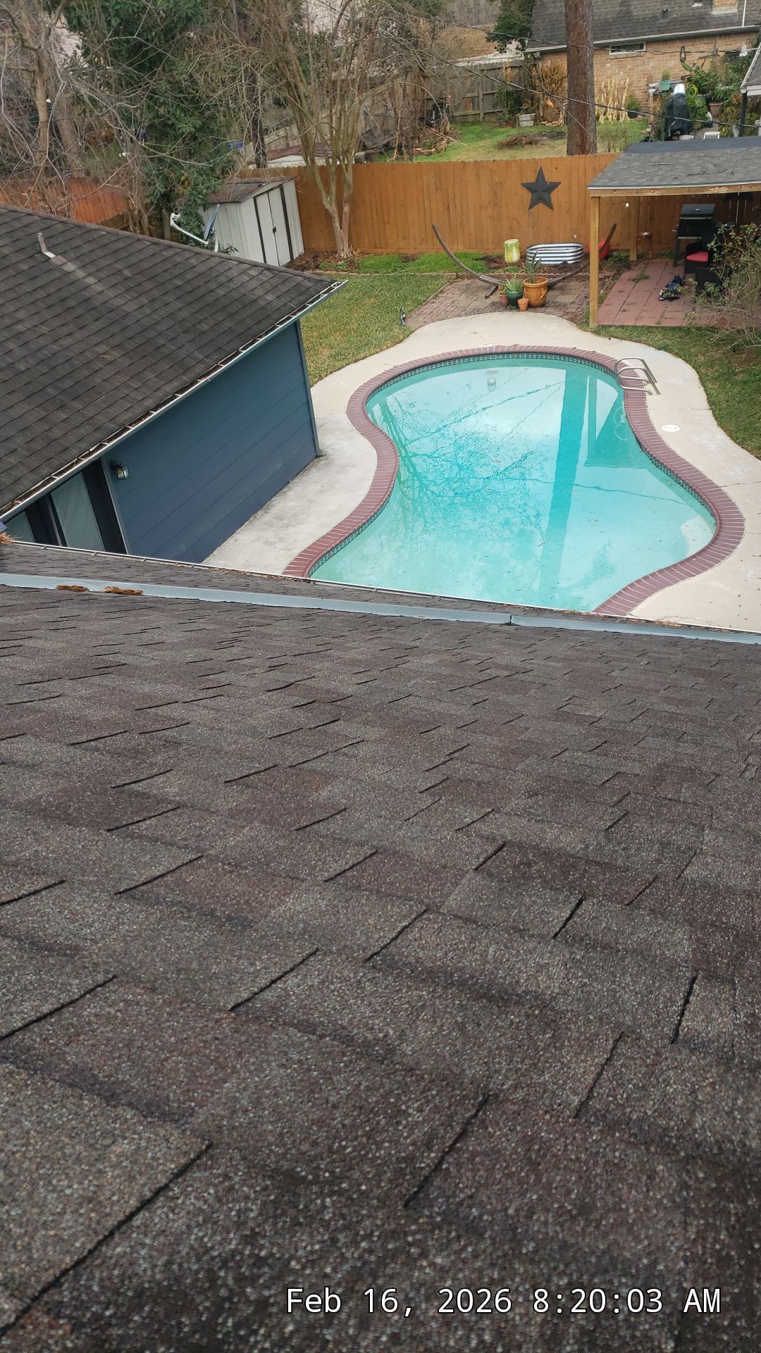 Backyard pool with turquoise water beside a house and wooden fence, viewed from a shingled roof
