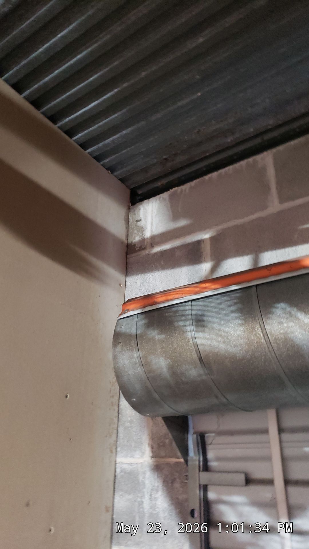 Industrial ceiling with silver ventilation duct and corrugated metal roof in a beige room
